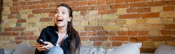 Panoramic orientation of young excited woman holding remote controller while watching movie — Stock Photo