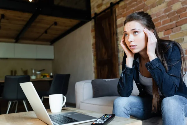 Messa a fuoco selettiva di concentrata ragazza toccare la testa durante la visione di film vicino computer portatile e tazza — Foto stock