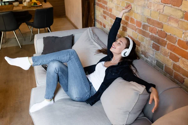 Cheerful girl in wireless headphones listening music in living room — Stock Photo