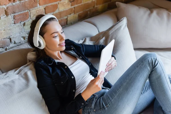 Chica alegre en auriculares inalámbricos escuchar música y el uso de la tableta digital - foto de stock