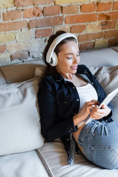 Chica feliz en auriculares inalámbricos escuchando música y usando tableta digital - foto de stock