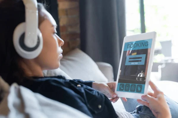 Messa a fuoco selettiva della ragazza in cuffie wireless ascoltare musica e utilizzando tablet digitale con app di prenotazione — Foto stock