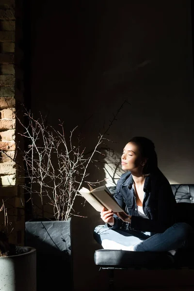 Luz del sol sobre la joven alegre con los ojos cerrados sosteniendo libro - foto de stock