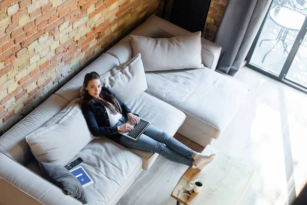 KYIV, UKRAINE - APRIL 29, 2020: overhead view of attractive freelancer using laptop near digital tablet with facebook app — Stock Photo