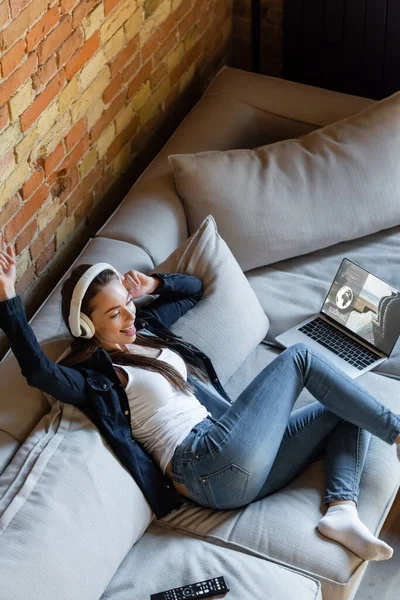 Overhead view of happy woman listening music in wireless headphones near laptop with tickets website — Stock Photo