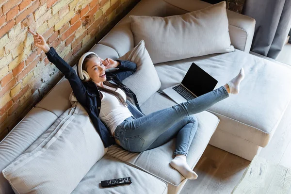 Visão aérea da menina feliz ouvir música em fones de ouvido sem fio perto de laptop com tela em branco e controle remoto — Fotografia de Stock