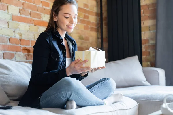 Attraktive Frau sitzt auf Sofa und hält Geschenkbox — Stockfoto