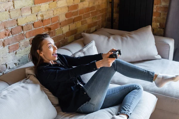 KYIV, UKRAINE - 29 AVRIL 2020 : femme joyeuse tenant un joystick tout en jouant au jeu vidéo dans le salon — Photo de stock