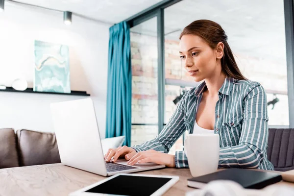 Selective focus of beautiful freelancer using laptop near digital tablet with blank screen — Stock Photo