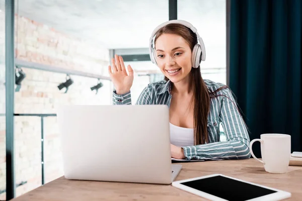 Foyer sélectif de la fille dans les écouteurs sans fil agitant la main près de l'ordinateur portable et tablette numérique avec écran vide — Photo de stock