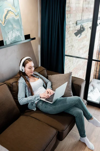 Freelancer atraente em fones de ouvido sem fio usando laptop na sala de estar — Fotografia de Stock