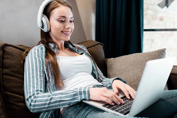 Enfoque selectivo de freelancer feliz en auriculares inalámbricos utilizando el ordenador portátil en la sala de estar - foto de stock