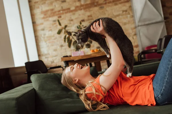 Excited woman lying on sofa and holding in arms cute cat — Stock Photo