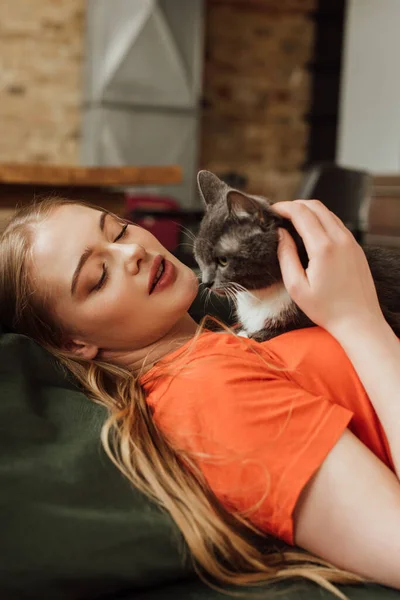 Attraktive junge Frau schaut niedliche Katze im Wohnzimmer an — Stockfoto