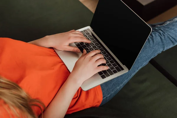 Vista recortada de un joven freelancer usando un portátil con pantalla en blanco en la sala de estar - foto de stock