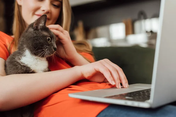 Corte vista de freelancer sorrindo usando laptop e tocando gato bonito na sala de estar — Fotografia de Stock