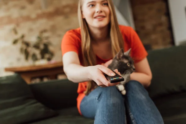 Enfoque selectivo de la chica feliz sosteniendo el mando a distancia cerca de gato lindo - foto de stock