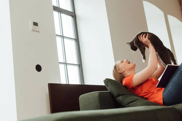 Enfoque selectivo de excitado joven mujer sosteniendo en brazos lindo gato en sala de estar - foto de stock