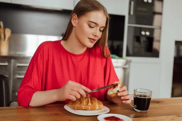 Attraktives Mädchen hält Messer mit süßer Marmelade in der Nähe von leckerem Croissant — Stockfoto