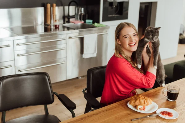 Feliz jovem mulher segurando bonito gato perto saboroso café da manhã — Fotografia de Stock