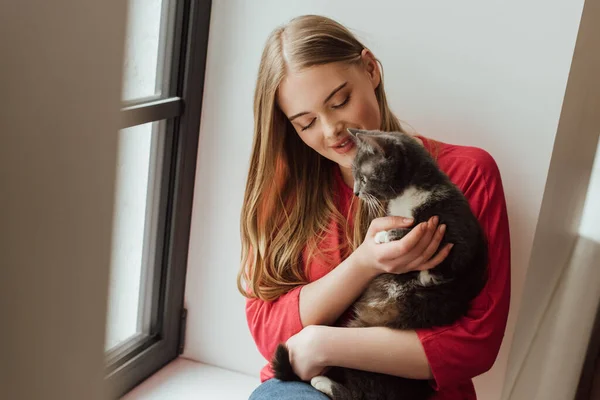 Selective focus of young woman looking at cute cat near window — Stock Photo