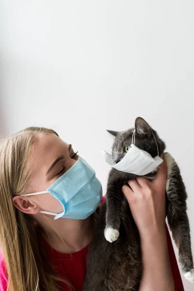 Femme femme tenant dans les bras chat mignon dans le masque médical près du mur blanc — Photo de stock