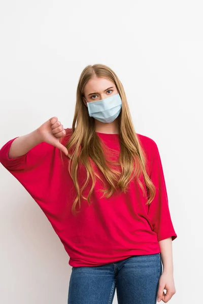 Giovane donna in maschera medica mostrando pollice verso il basso isolato su bianco — Foto stock