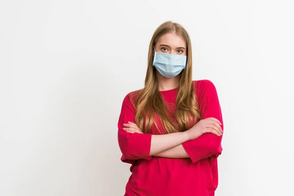 Jovem mulher em máscara médica de pé com os braços cruzados isolados em branco — Fotografia de Stock