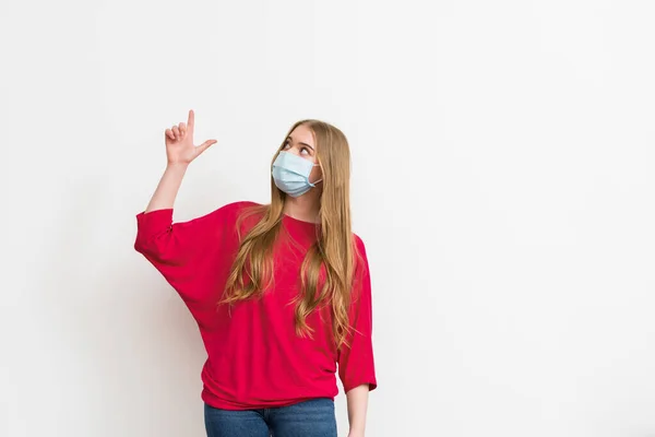 Femme dans le masque médical pointant avec le doigt et regardant vers le haut isolé sur blanc — Photo de stock