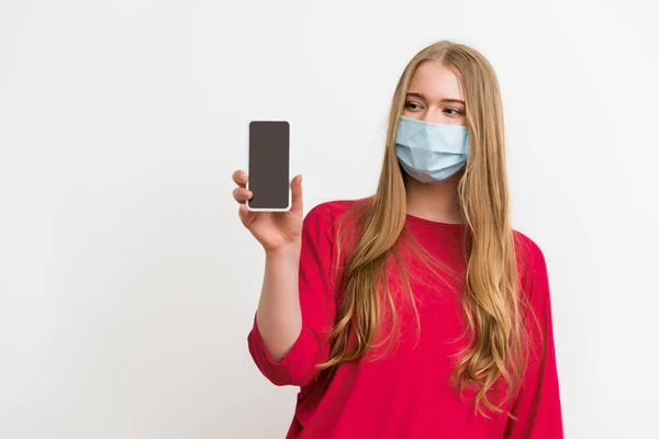 Mulher em máscara médica olhando para smartphone com tela em branco isolado no branco — Fotografia de Stock