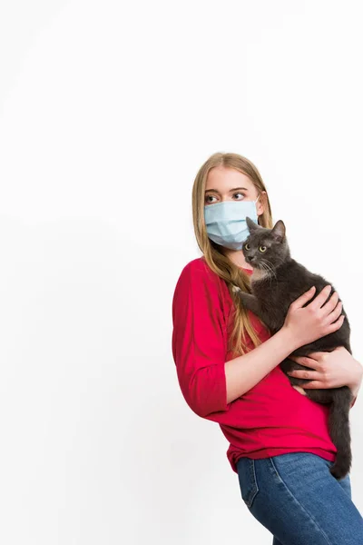 Young woman in medical mask holding in arms cute cat isolated on white — Stock Photo