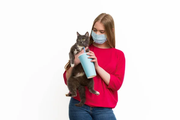 Femme dans le masque médical tenant dans les bras mignon chat et tasse jetable avec soda isolé sur blanc — Photo de stock