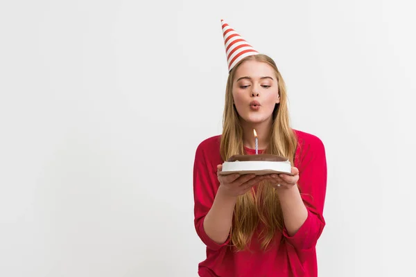 Jolie fille en chapeau de fête soufflant bougie sur gâteau d'anniversaire isolé sur blanc — Photo de stock