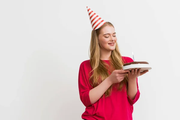 Cheerful girl in party cap smiling and looking at birthday cake isolated on white — Stock Photo