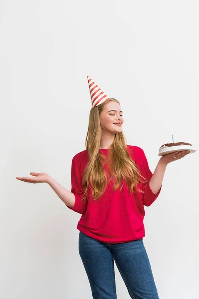 Молода жінка у вечірній кепці тримає торт на день народження та жестикулює ізольовано на білому — стокове фото
