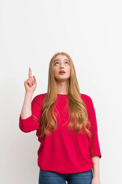 Mujer sorprendida señalando con el dedo mientras mira hacia arriba aislado en blanco - foto de stock