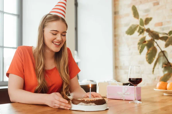 Cheerful woman in party cap looking at delicious birthday cake — Stock Photo