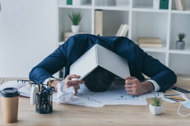 depressed businessman covering head with laptop while sitting at workplace clipart