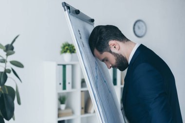 depressed businessman standing with closed eyes and leaning at flipchart with forehead  clipart