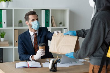 Ofisteki tıbbi maskeli iş adamına kağıt torba veren yemek dağıtıcısının kısmi görüntüsü