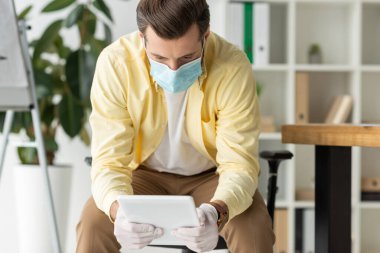 Ofiste dijital tablet kullanan tıbbi maskeli ve lateks eldivenli iş adamı