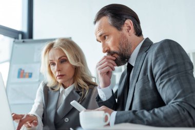 Bilgisayarlı seçici iş kadını odaklı. Düşünceli iş adamının yanında çalışıyor. Kahve fincanının yanında akıllı telefonu var. 