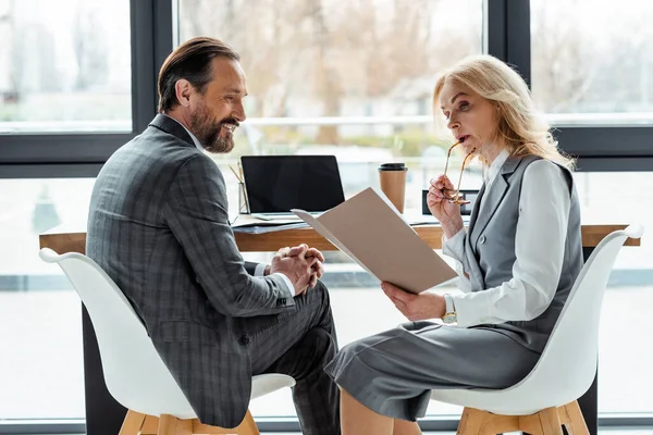 Seitenansicht Einer Geschäftsfrau Mit Papiermappe Der Nähe Eines Lächelnden Geschäftsmanns — Stockfoto