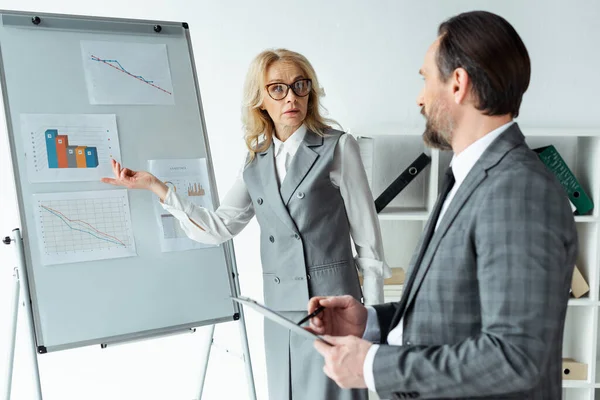 オフィスでクリップボードとビジネスマンの近くのホワイトボード上のグラフを指すビジネスマンの選択的な焦点 — ストック写真