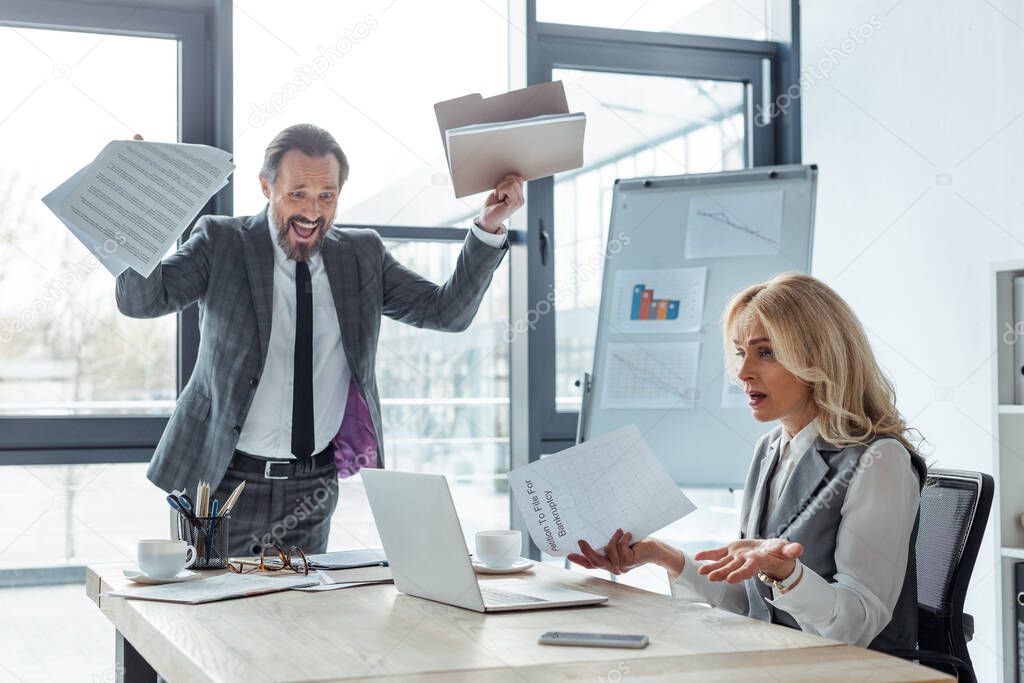 Confused businesswoman holding petition to file to bankruptcy near cheerful businessman holding documents in office 