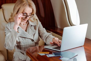 Selective focus of businesswoman using laptop near credit cards and passports with air tickets on table in plane  clipart