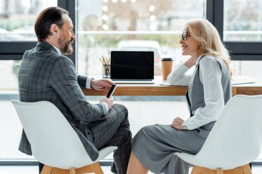 Ofisteki masanın yanındaki bilgisayarın yanında iş adamına gülümseyen iş kadınının yan görüntüsü 