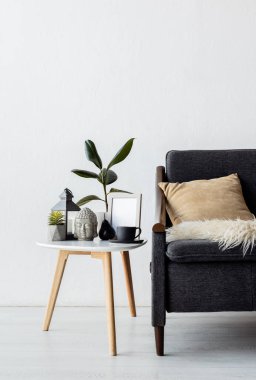 pillow on modern sofa near coffee table with plants, vintage lamp, head figurine and cup in living room  clipart