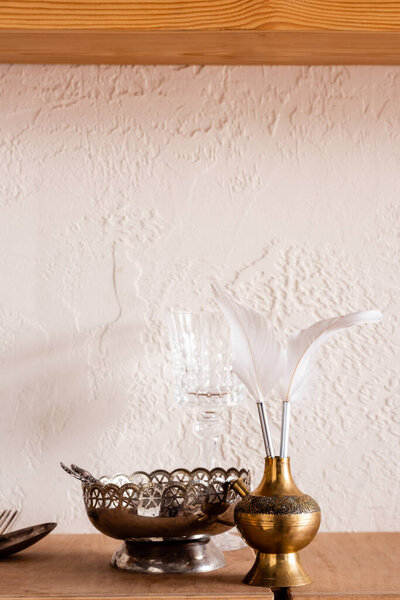 silver bowl near white feathers in vintage vase 