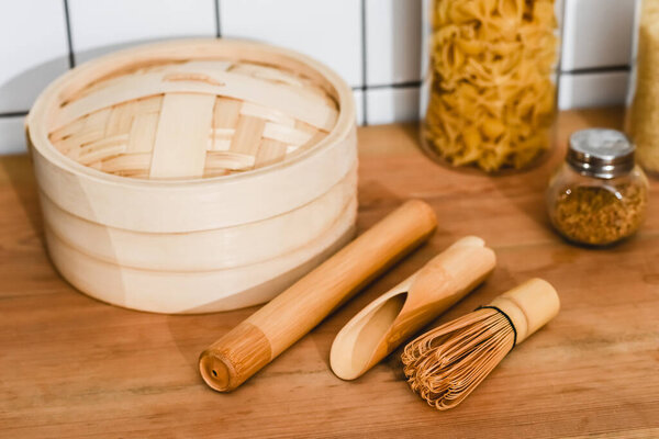 selective focus of bamboo steamer near cooking utensils and jars with dried pasta